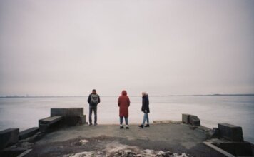Трое обвиняемых по делу о похищении и ограблении в Калгари Three individuals are standing on a pier overlooking a frozen lake on a cloudy winter day.