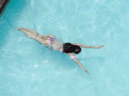 Top view of anonymous slim lady floating underwater in crystal clear blue water in swimming pool on resort