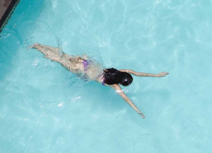 Top view of anonymous slim lady floating underwater in crystal clear blue water in swimming pool on resort