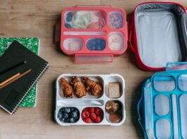 Top view of composed plastic lunchboxes near copybooks under pencils on wooden table