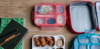 Top view of composed plastic lunchboxes near copybooks under pencils on wooden table