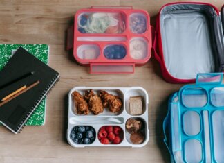 Top view of composed plastic lunchboxes near copybooks under pencils on wooden table