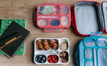 Top view of composed plastic lunchboxes near copybooks under pencils on wooden table