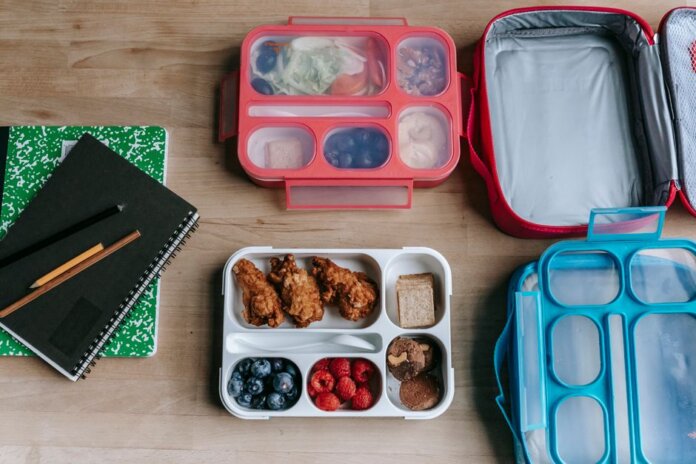 Top view of composed plastic lunchboxes near copybooks under pencils on wooden table