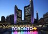 Toronto City Hall illuminated at twilight with colorful Toronto sign in the foreground.