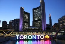 Toronto City Hall illuminated at twilight with colorful Toronto sign in the foreground.