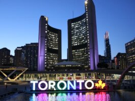 Toronto City Hall illuminated at twilight with colorful Toronto sign in the foreground.
