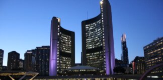 Toronto City Hall illuminated at twilight with colorful Toronto sign in the foreground.