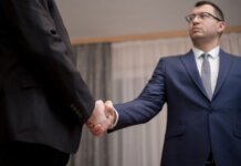 Two businessmen in formal attire shaking hands during a meeting.