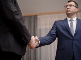 Two businessmen in formal attire shaking hands during a meeting.