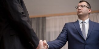 Two businessmen in formal attire shaking hands during a meeting.