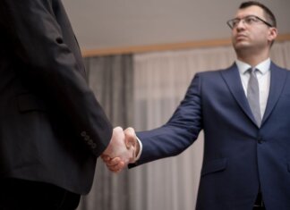 Two businessmen in formal attire shaking hands during a meeting.