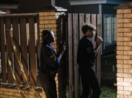 Two police officers investigate a crime scene at night, entering a house with caution.