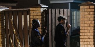 Two police officers investigate a crime scene at night, entering a house with caution.