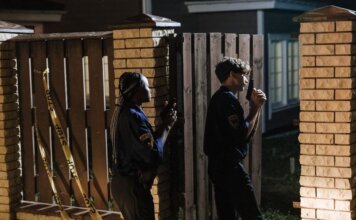 Two police officers investigate a crime scene at night, entering a house with caution.