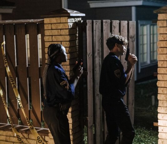 Two police officers investigate a crime scene at night, entering a house with caution.