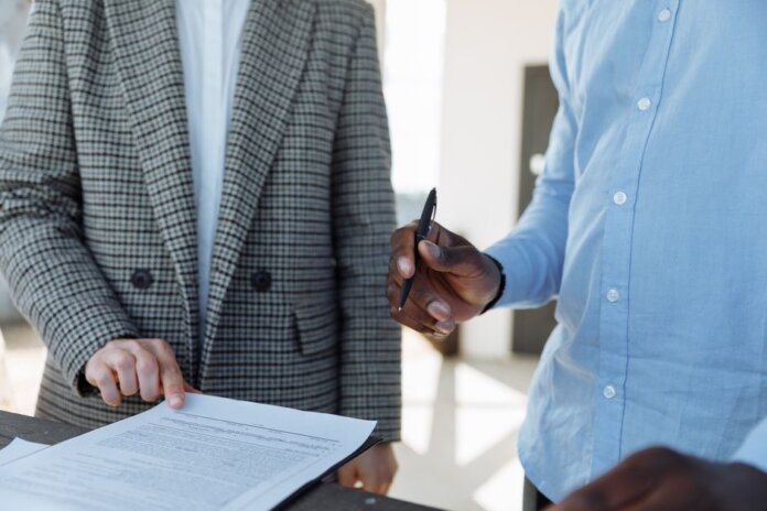 Two professionals reviewing business documents and discussing details in an office setting. Two professionals reviewing business documents and discussing details in an office setting.