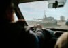 View from inside a car driving past a military tank on a road in Ukraine.
