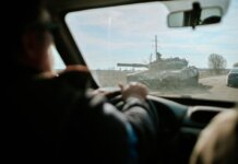 View from inside a car driving past a military tank on a road in Ukraine.