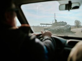 View from inside a car driving past a military tank on a road in Ukraine.