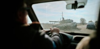 View from inside a car driving past a military tank on a road in Ukraine.