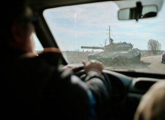 Украинские дроны бьют по России, но Путин не откажется от войны View from inside a car driving past a military tank on a road in Ukraine.