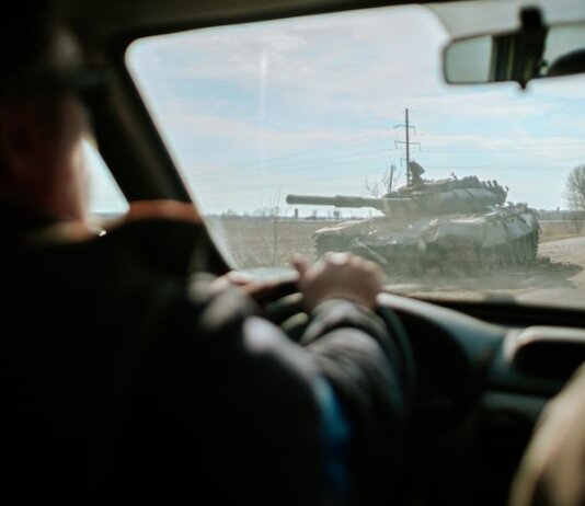 View from inside a car driving past a military tank on a road in Ukraine.
