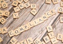 Wooden letter tiles forming the word 'COMPLIANCE' on a rustic wooden background.