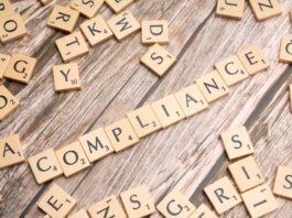 Wooden letter tiles forming the word 'COMPLIANCE' on a rustic wooden background.