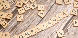 Wooden letter tiles forming the word 'COMPLIANCE' on a rustic wooden background.