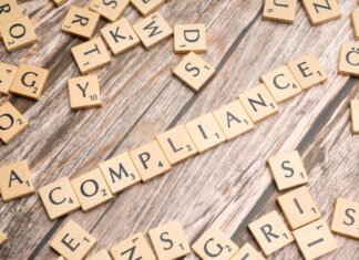 Wooden letter tiles forming the word 'COMPLIANCE' on a rustic wooden background.