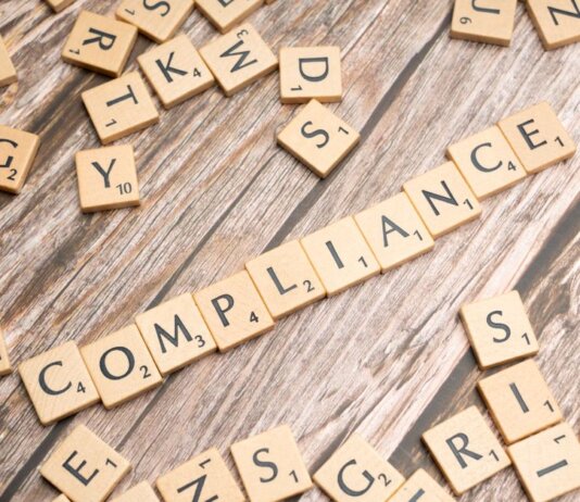 Wooden letter tiles forming the word 'COMPLIANCE' on a rustic wooden background.
