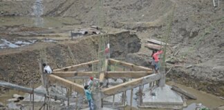 Workers constructing a building foundation with rebar and wooden supports outdoors.