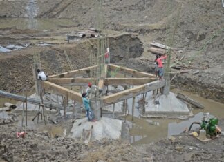 Workers constructing a building foundation with rebar and wooden supports outdoors.