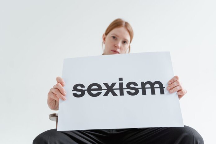 A caucasian woman confidently holds a sign addressing sexism in a bright studio setting. A caucasian woman confidently holds a sign addressing sexism in a bright studio setting.