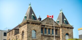 A classic stone courthouse in Nanaimo, British Columbia, with Canadian flag, under clear blue sky.