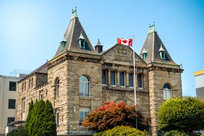 A classic stone courthouse in Nanaimo, British Columbia, with Canadian flag, under clear blue sky. A classic stone courthouse in Nanaimo, British Columbia, with Canadian flag, under clear blue sky.