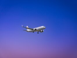 A commercial airplane flying through a clear blue and purple sky during daytime.
