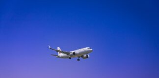 A commercial airplane flying through a clear blue and purple sky during daytime.