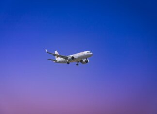 A commercial airplane flying through a clear blue and purple sky during daytime.