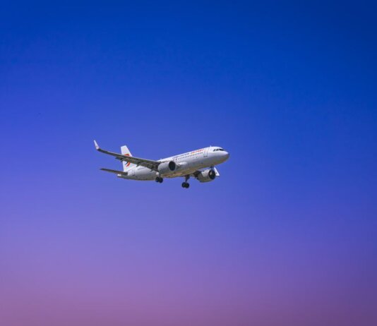 A commercial airplane flying through a clear blue and purple sky during daytime.