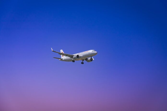 A commercial airplane flying through a clear blue and purple sky during daytime.