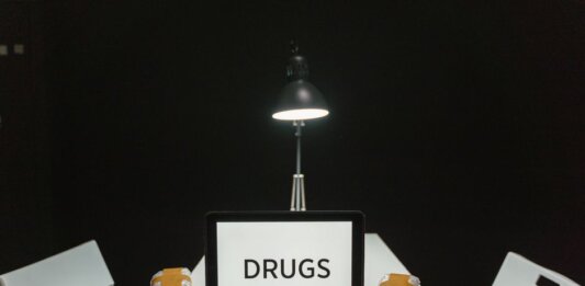 A dimly lit room with a sign displaying 'DRUGS' surrounded by money and illegal substances.