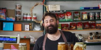 A friendly shopkeeper stands behind shelves of homemade preserves.