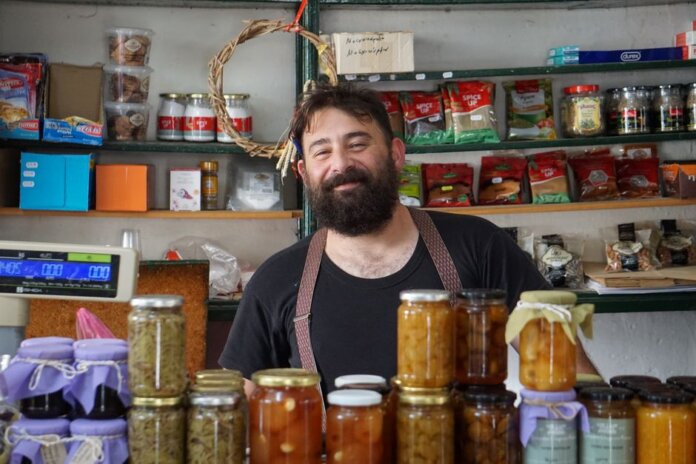 A friendly shopkeeper stands behind shelves of homemade preserves. A friendly shopkeeper stands behind shelves of homemade preserves.