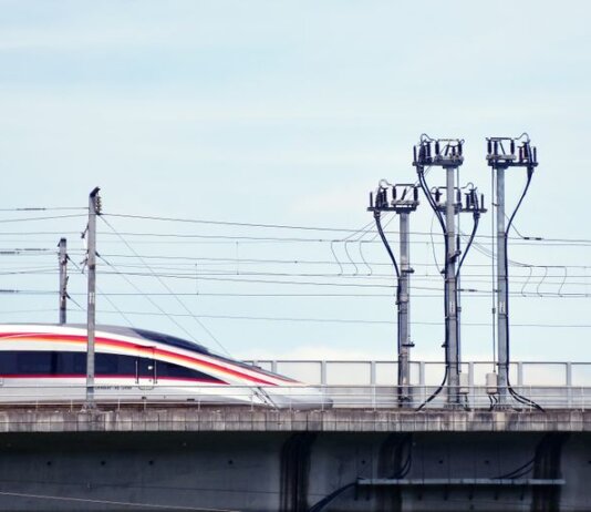 A high-speed train moves swiftly on an elevated railway under a clear sky.