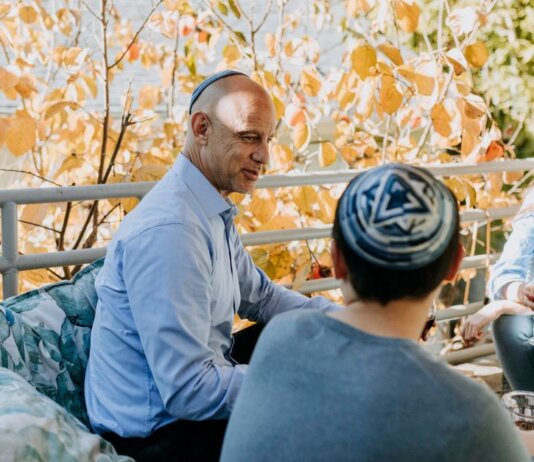 A Jewish family enjoying a festive outdoor gathering during fall, sharing talks and wine.