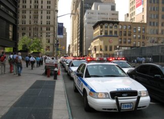 Пьер Пуалиевр едет в Нью-Йорк отстаивать безтарифную торговлю A line of NYPD police cars with flashing lights on a busy New York street, featuring pedestrians and tall buildings.