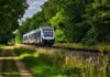 A modern passenger train moving through a scenic, green countryside, emphasizing travel and transportation.