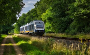 A modern passenger train moving through a scenic, green countryside, emphasizing travel and transportation.